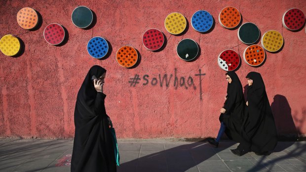 Iranians walk past a decorated wall on a quiet street in downtown Tehran, Iran, on Wednesday.