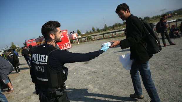 Warm welcome ... A Berlin policeman gives water to a migrant who had arrived on a chartered train from Munich at Schoenefeld train station on Thursday in Germany. 