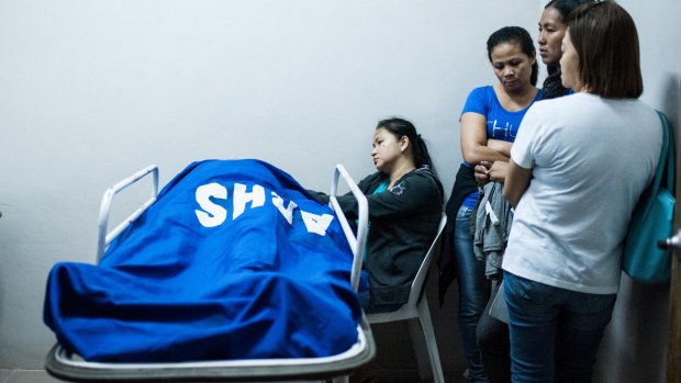 Relatives stand beside the body of a police intelligence officer killed during a botched drug raid which also killed three drug suspects on August 20.