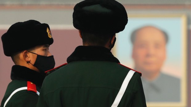 Chinese paramilitary policemen wearing protection masks stand watch over visitors near a portrait of Mao Zedong on Tiananmen Square in Beijing.