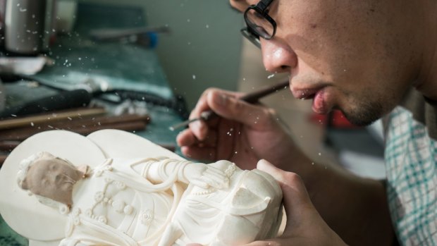 Ivory dust flies as Zhang Yong blows it away during carving at Li Chunke's ivory carving workshop in Beijing on Monday.