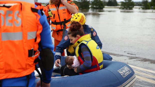 A young mother and her seriously ill four-month old baby are taken across the flooded Cessnock Road in an inflatable boat.