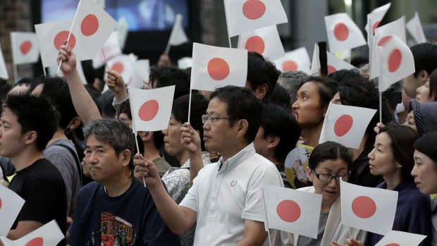 Attendees hold Japanese national flags as they wait for the arrival of PM Shinzo Abe.