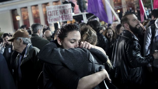 Syriza supporters embrace after the results are announced. A sign in the background says "Good night Mrs Merkel" in German.