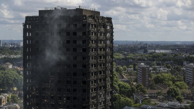 Debris hangs from the blackened exterior as smoke continues to rise from Grenfell Tower on Thursday.
