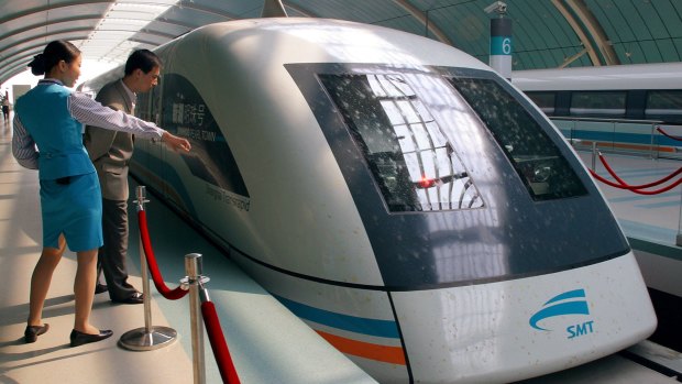 A station worker guides a passenger near a Maglev train.