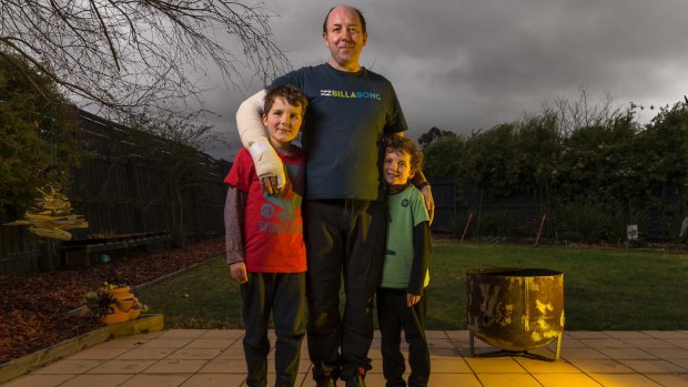 Good to have Dad home: Burns patient Brett Mumford in his Taylors Lakes backyard on Sunday with sons Jarvis, 8, (left) and Casey, 7, and the fire pit (right) that Mr Mumford unwisely poured petrol into.  