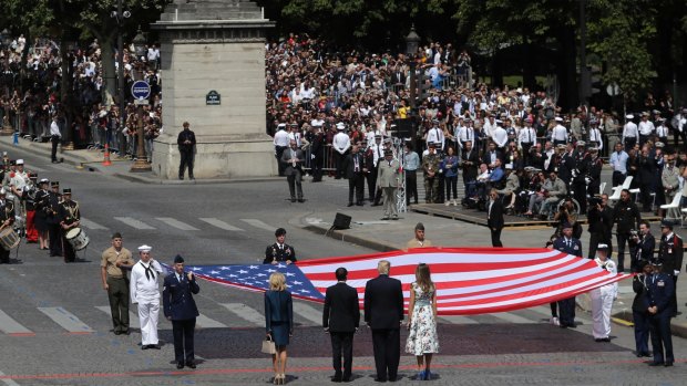 The two presidential couples stand in front of a huge American flag after the Bastille Day parade in Paris, on Friday.