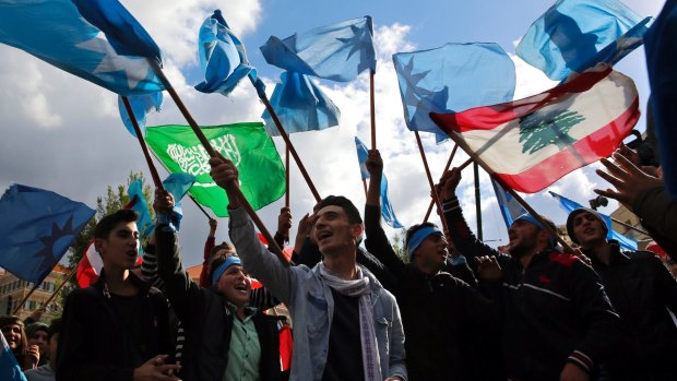 Supporters of Lebanese Prime Minister Saad Hariri rally outside his house holding the flags of Saudi Arabia, left, Lebanon and the blue flag of Hariri's Future Movement.