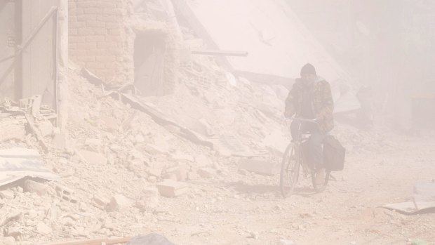 A Syrian man rides his bicycle through smoke and dust after an Assad regime air strike on residential areas of Douma, Damascus, last week.