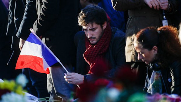 A mourner holds a French national flag as he pays his respects to victims of the terrorist attacks, at Place de la Republique in Paris.