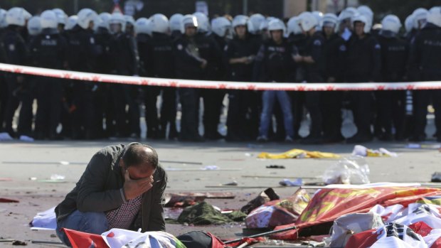 A man weeps over the body of a victim at the blast site as police look on.