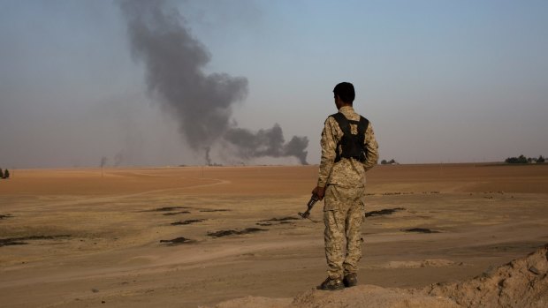 A member of an Arab tribal militia fighting the Islamic State group watches as smoke rises from a crude oil refinery in Tel al-ail, Syria.