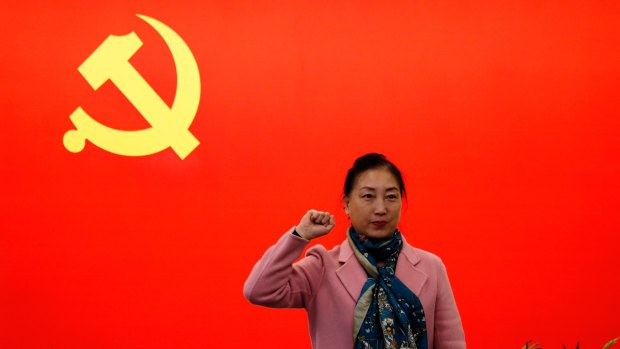 A woman poses for a photograph in front of a Communist flag on display in Shanghai, China. 