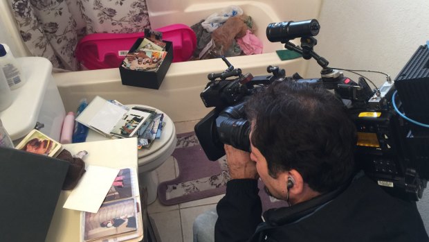 A cameraman films photo albums scattered on top of the toilet in the apartment.