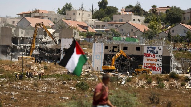 A Palestinian man holds the Palestinian flag as the Dreinoff buildings, which sit on land owned by Palestinians, are destroyed.