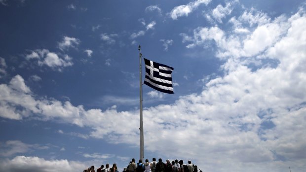 People stand under a Greek national flag atop the Acropolis hill in Athens yesterday. 