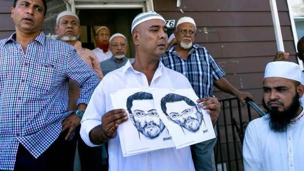 Worshippers outside the Ozone Park mosque hold a police sketch of a suspect wanted over the shooting of two men.