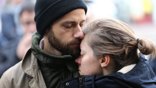 A couple embrace after laying flowers at the La Belle Equipe cafe