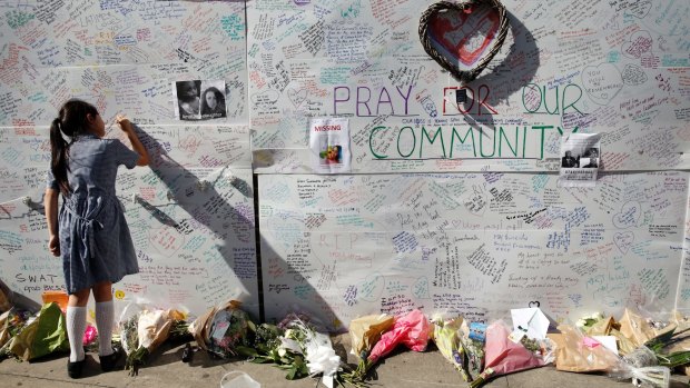 A school girl writes a message on a memorial wall.