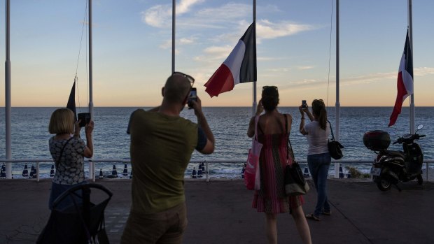 People take pictures of French flags flying at half mast on the Promenade des Anglais on Friday.