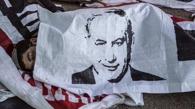 An Israeli settler sleeps under a banner depiciting Prime Minister Benjamin Netanyahu after an overnight standoff with police in the occupied West Bank.