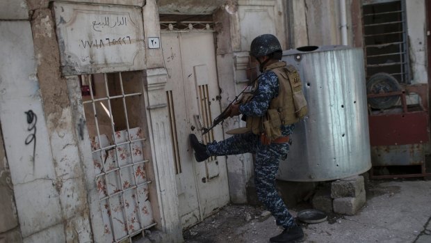 An Iraqi policeman kicks open the door of a house as fighting against IS militants continues on the western side of Mosul on Monday.