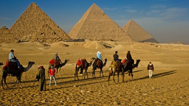 Tourists ride camels past the Pyramids of Giza.