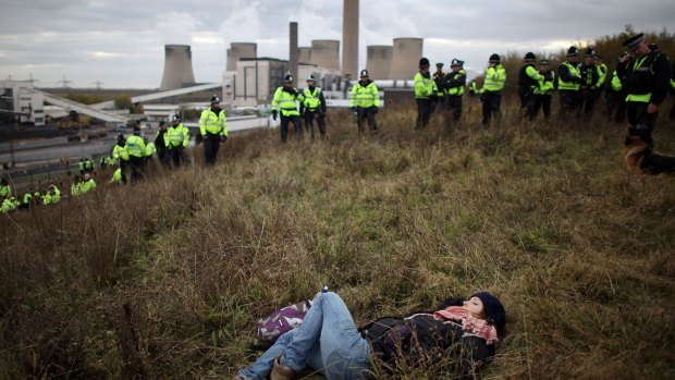 A British anti-coal power protester sleeps as police officers form a line during a climate change demonstration at Ratcliffe Power Station in England.