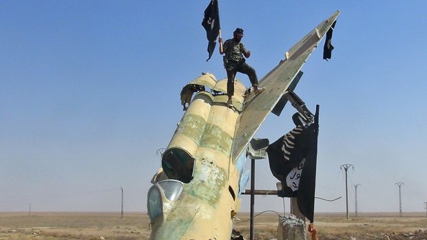 Fghters of the Islamic State wave the group's flag from a damaged display of a government fighter jet following the battle for the Tabqa air base, in Raqqa, Syria, in 2014.