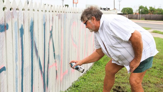 Graham Wilson of Bowen paints a fresh message on his fence in the wake of Cyclone Debbie.