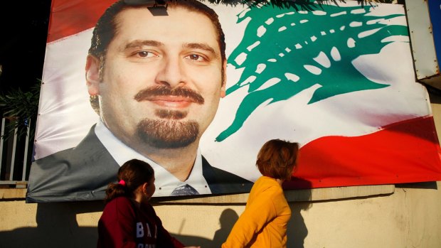 A woman and her daughter pass by a poster of outgoing Prime Minister Saad Hariri, in Beirut, Lebanon.