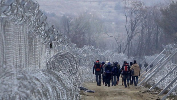 Refugees and migrants, who entered Macedonia from Greece illegally, walk between the two lines of the protective fence along the border line, near southern Macedonia's town of Gevgelija.