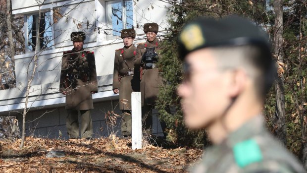 North Korean soldiers look at a South Korean guard standing near the spot where a North Korean soldier crossed the border in the Demilitarised Zone on November 13.