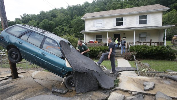Jay Bennett, left, and step-son Easton Phillips survey the damage to a neighbors car in front of their home damaged by floodwaters as the cleanup begins from severe flooding in White Sulphur Springs, West Virginia. 