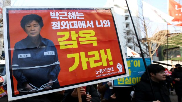 A demonstrator demanding South Korean President Park Geun-hye's impeachment holds a sign featuring a photograph of Park during a protest on Friday.
