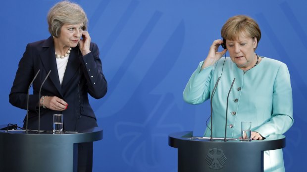 German Chancellor Angela Merkel, right, and British Prime Minister Theresa May hold their earphones during a joint news conference in Berlin.