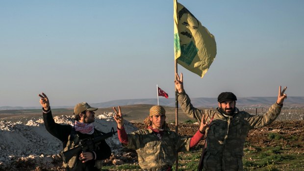 Members of the YPG militia beside a flag depicting jailed PKK leader Abdullah Ocalan in Aleppo province, Syria. Behind them is a flag flying over a Turkish enclave in Syria.