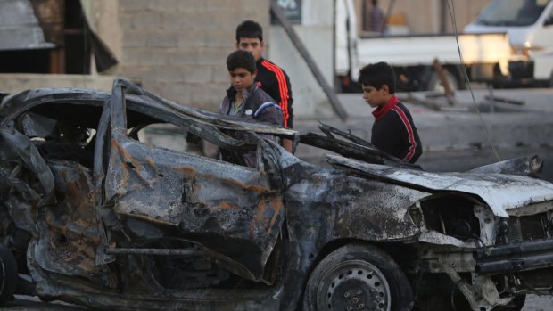 Fear factor: Iraqi children stand near a car destroyed by a bomb in the mostly Shiite district of Sadr City in northern Baghdad last week.