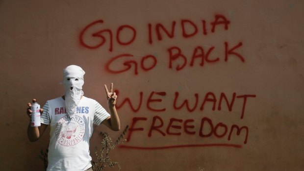 A masked Kashmiri protester in front of graffiti on the wall of a building in Srinagar.