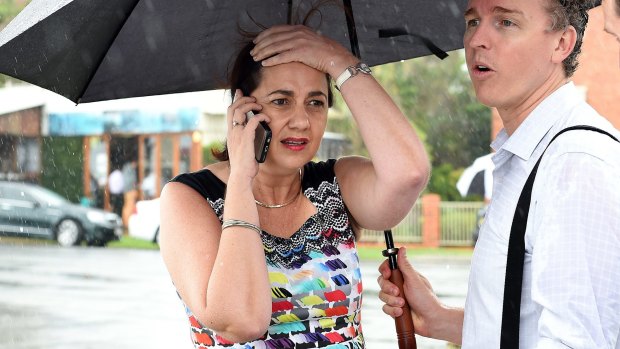 Queensland Premier Annastacia Palaszczuk is shielded from the rain by her media advisor as she takes a phone call.