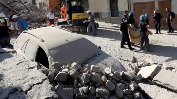 A body is carried away as a car is covered in rubble after an earthquake, in Amatrice, central Italy.