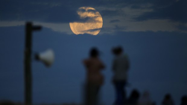 People watch as the super moon rises out of the clouds at Wanda Beach, Cronulla.