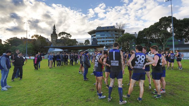 The crowd hovers around the huddle at a University Blues home match at University Oval.