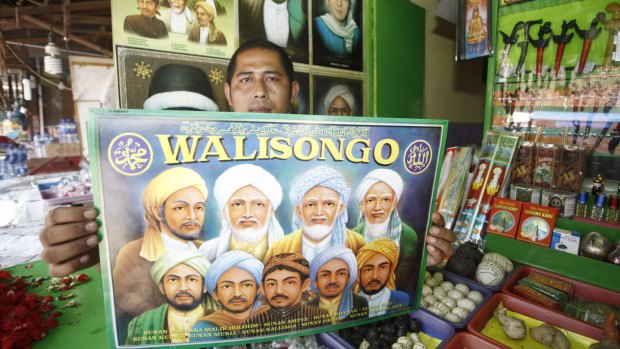 A vendor of merchandise at the shrine with a poster of the Wali Songo, or nine saints, credited with bringing Islam to Java.
