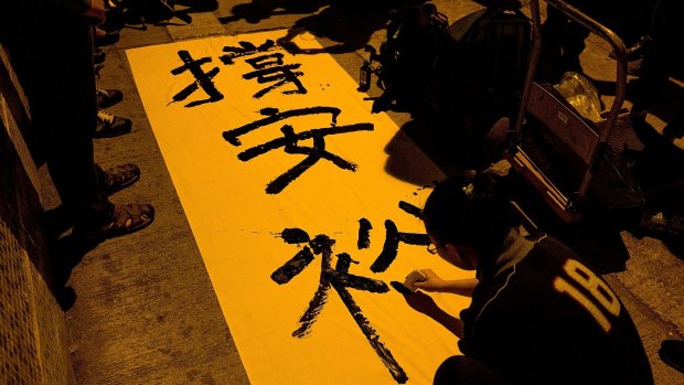 A supporter writes a slogan on a banner outside Ming Pao headquarters.