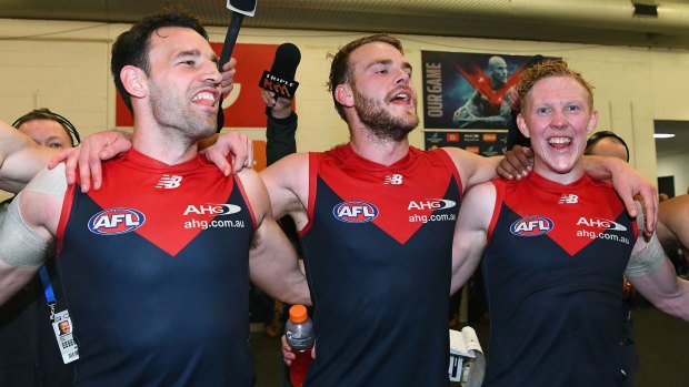Cameron Pedersen, Jack Watts and Clayton Oliver of the Demons sing the song in the rooms after a wonderful win. 