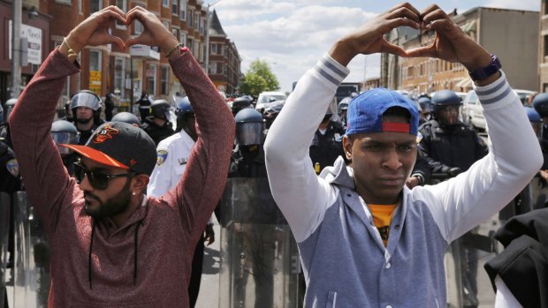 Baltimore peacemakers make heart gestures with their hands as they stand between riot police and rioters.