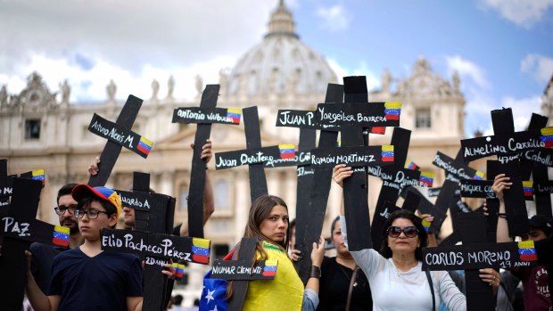 Demonstrators, in the Vatican, hold crosses adorned with the names of those killed in weeks of violent demonstrations calling on President Nicolas Maduro to step down.