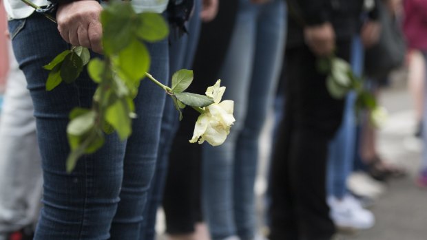 A woman holds a white rose as the hearses transporting coffins with the bodies of victims pass.